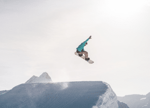 Čovjek na snowboardu sa planinom u pozadini i suncem