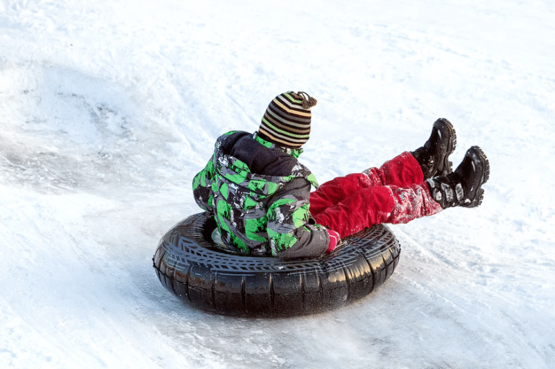 Dijete u zelenoj jakni i crvenim hlačama se igra po snijegu