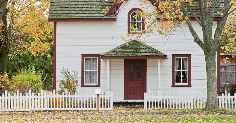 Bijela kuća sa bijelom ogradom i lišćem ispred kuće