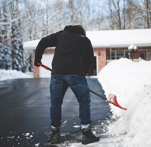 Čovjek koji čisti snijeg sa dvorišta u crnoj jakni i plavim hlačama sa lopatom