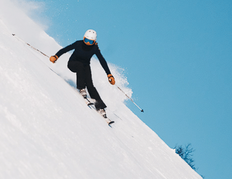 Čovjek koji skija sa bijelom kacigom i crnim odijelom niz planinu