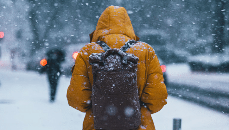 Čovjek sa narančastom jaknom i crnom torbom na snijegu