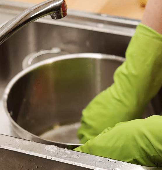 Osoba sa zelenim rukavicama koja pere suđe